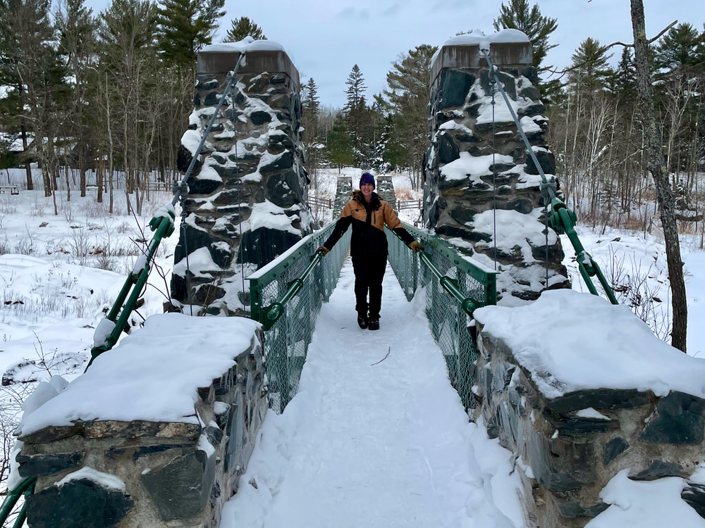 Woman stands in the middle of a snow covered suspension bridge