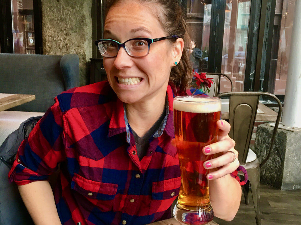 Woman wearing plaid shirt holds up a large ale in a Boston tavern