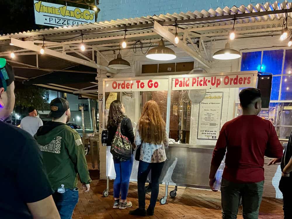 People stand in line to order at outdoor service window for a Savannah Georgia pizza parlor