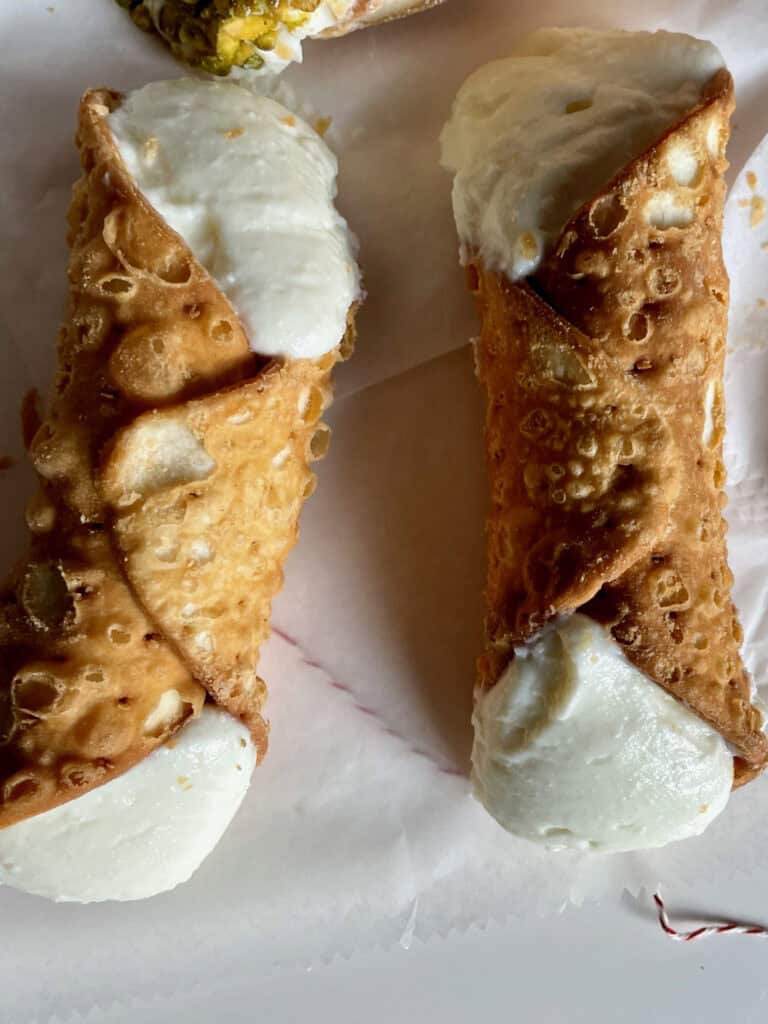 Two traditional cannoli sit on a paper liner.