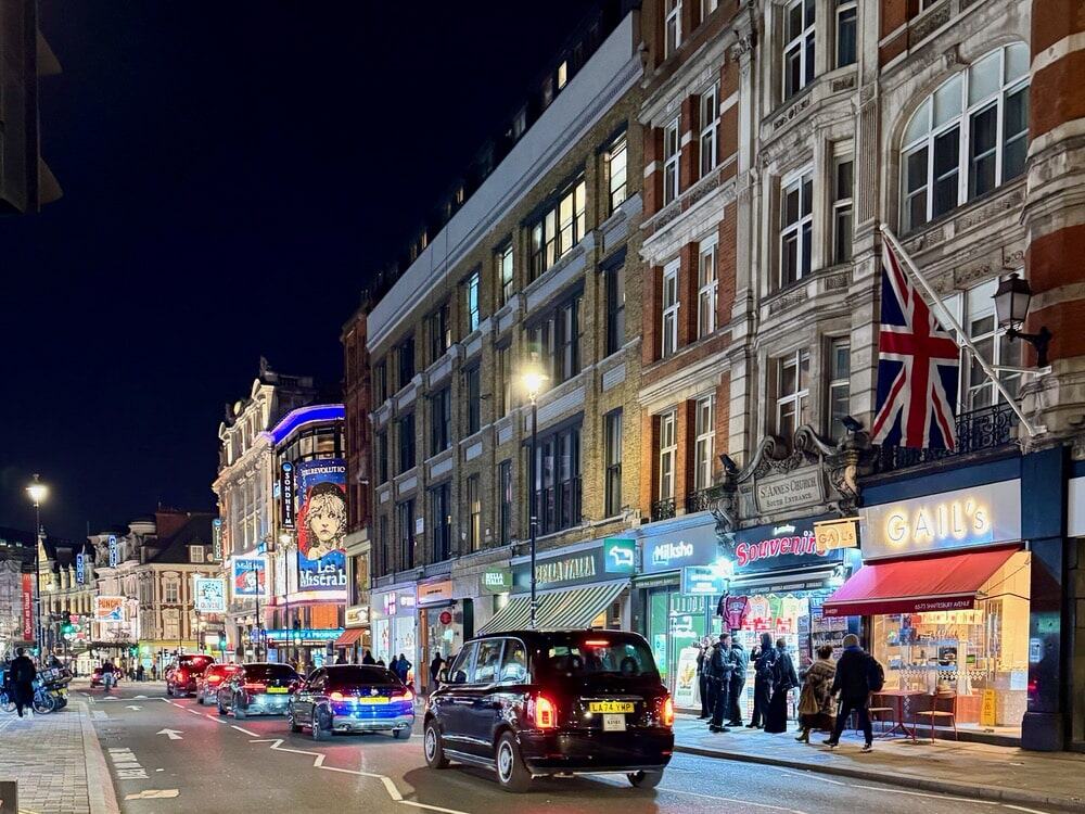 Taxis and vehicles on Shaftesbury Avenue London at night with bright theatre signs