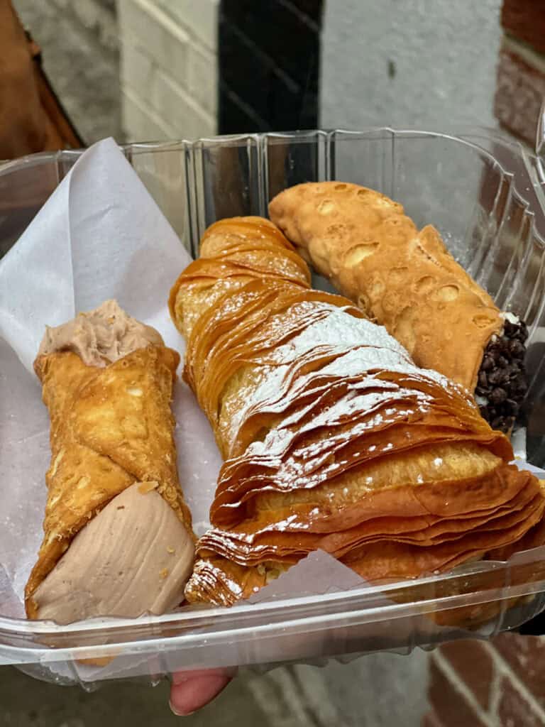 Three Italian pastries, two cannolis and one lobster tail, sit in a plastic clam shell case from a Boston bakery