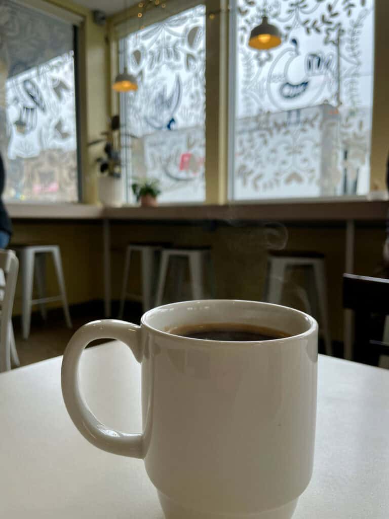 Full coffee cup sits in front of window decorated with decals