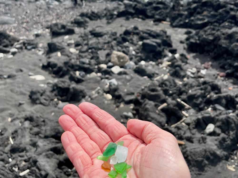 Hand folding bits of sea glass over a black sand beach in the Azores