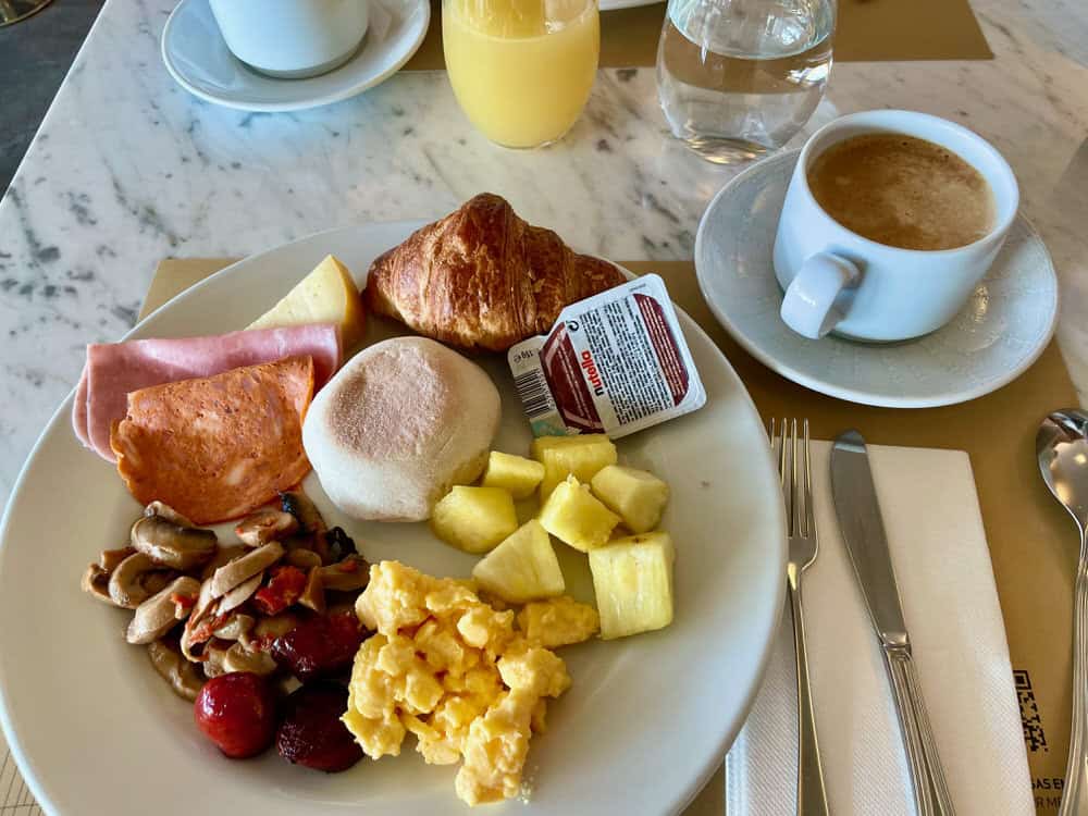 A plate of breakfast food including a bolo levedo bun and a cup of coffee
