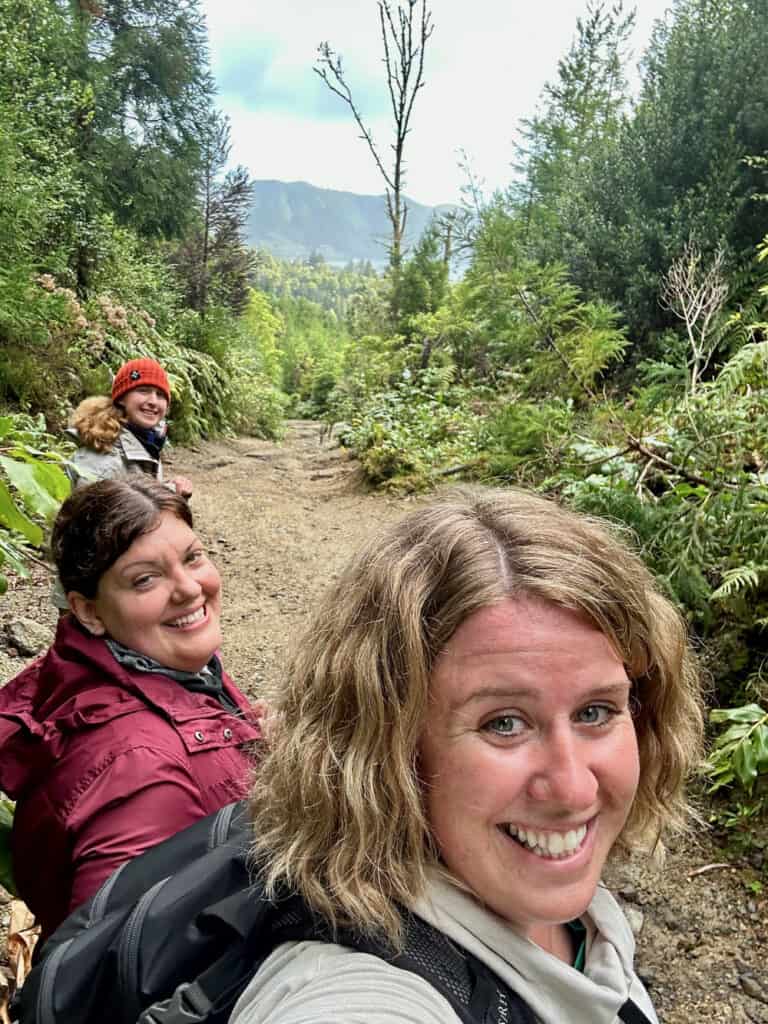 Three women pause on a dirt trail in the thick Azores forest