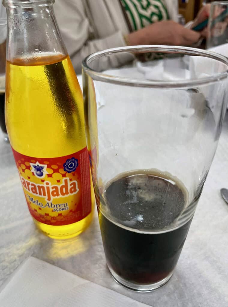 A bottle of orange sode and a partial glass of dark beer