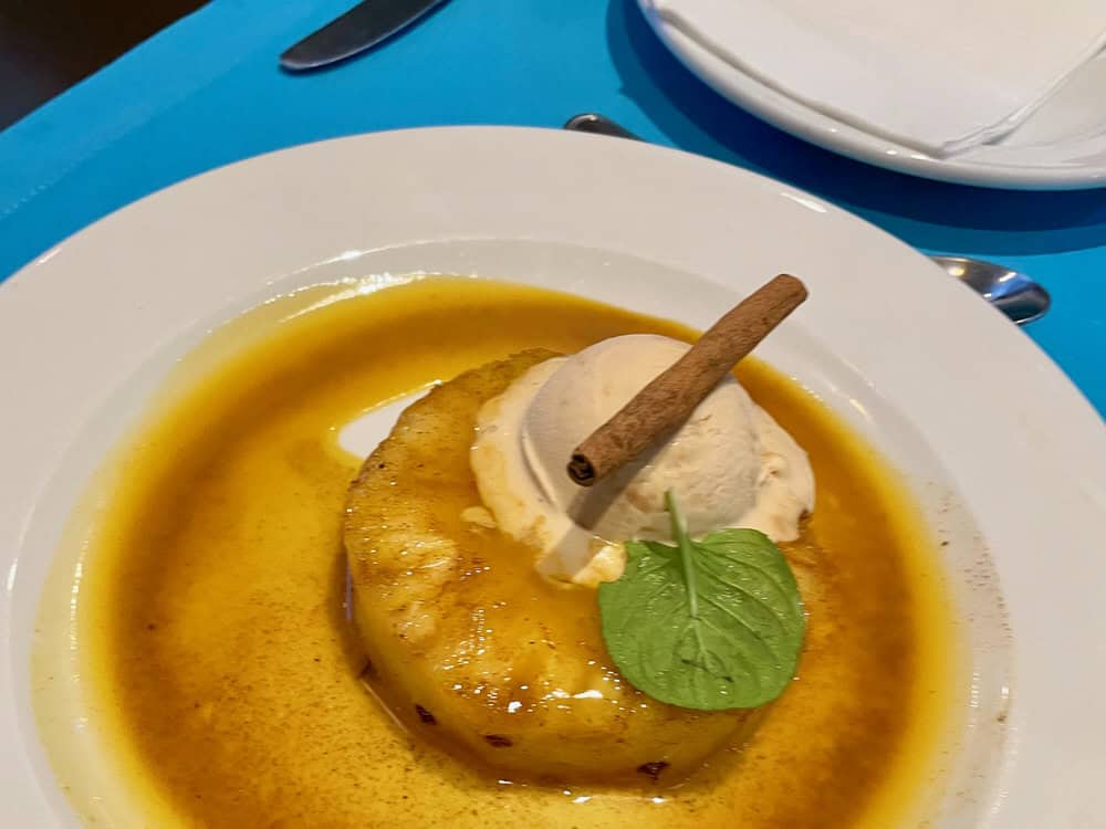 A piece of cooke pineapple topped with ice cream and sauce and garnished with a cinnamon stick and mint leaf