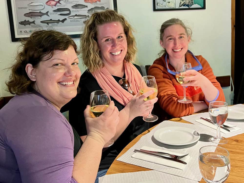 Three women hold glasses of white wine at a restaurant table in Ponta Delgada