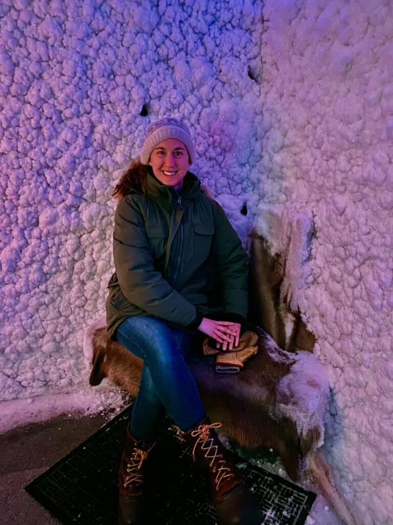 Woman dressed for winter sits against an icy wall