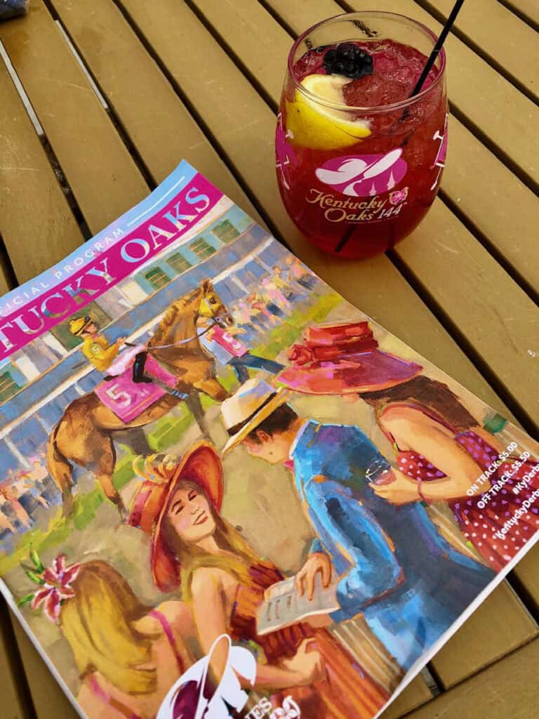 Colorful racetrack program sitting on a brown table with a red drink in a 144th Kentucky Oaks glass at Churchill Downs