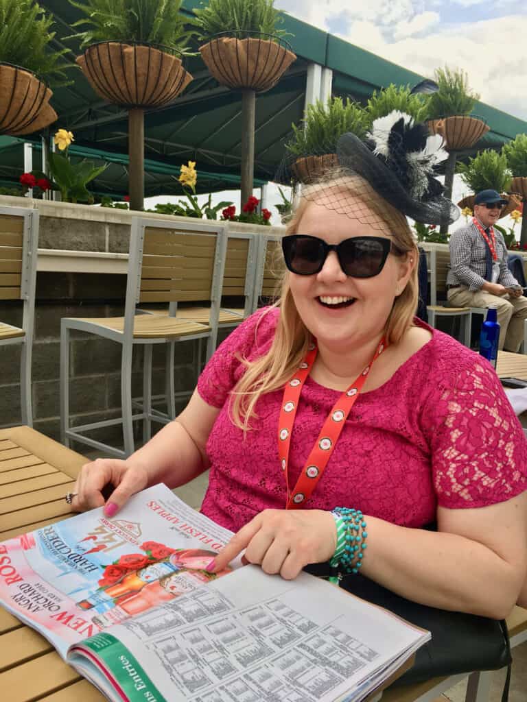 Woman wearing a fascinator and pink dress looks through a Kentucky Derby program