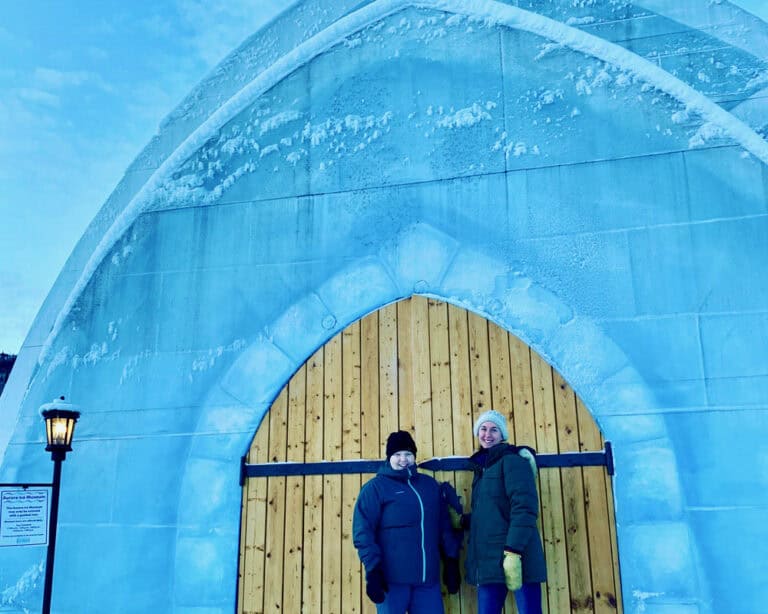 Two women stand at the entrance to an ice museum shaped like an igloo with Nordic style doors
