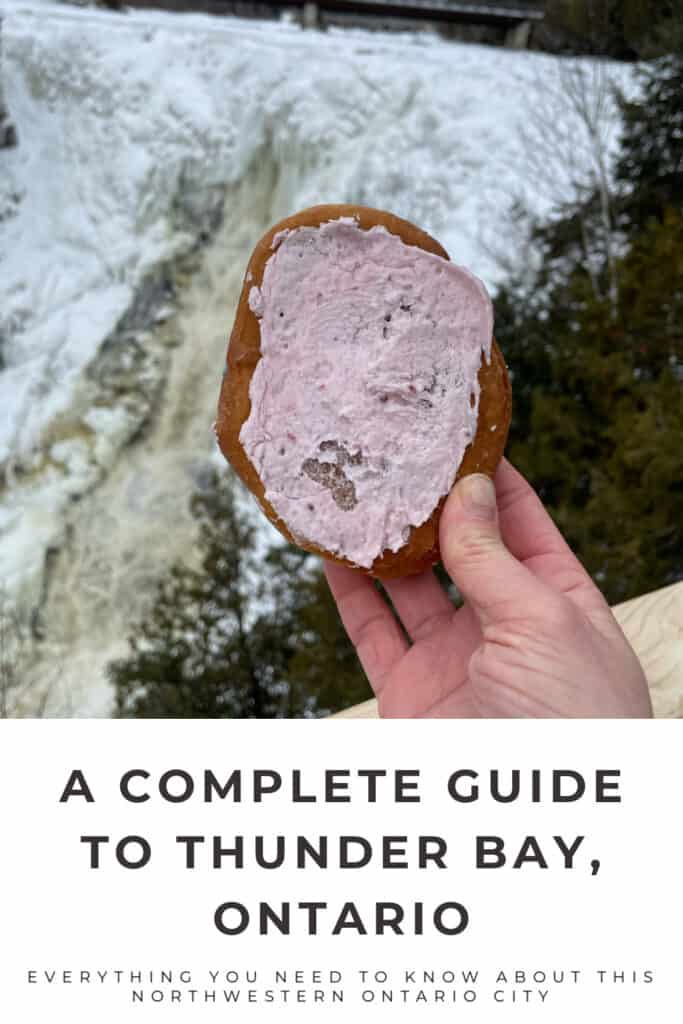 Hand holdng up a Persian donut in front of Kakabeka Falls in northwestern Ontario. Text reads "A Complete Guide to Thunder Bay, Ontario."