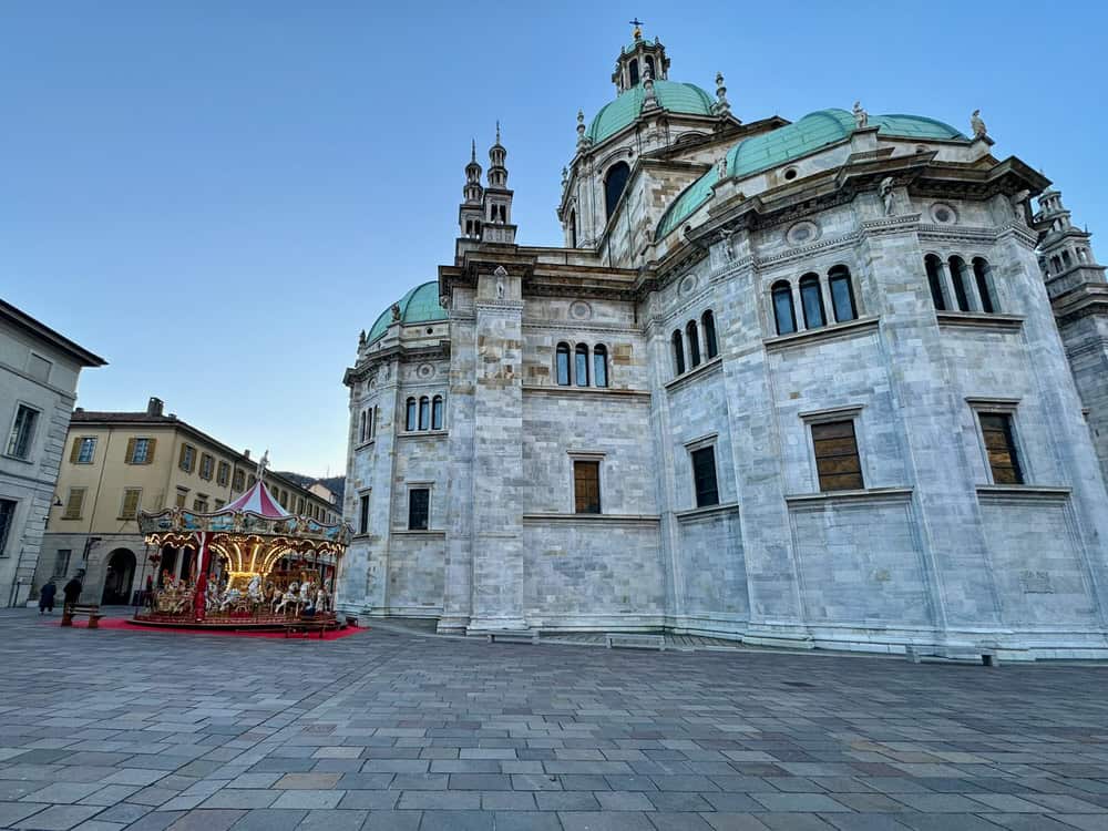 Back of Santa Maria Assunta Cathedral in Como Italy with a Christmas carousel set up in front of it