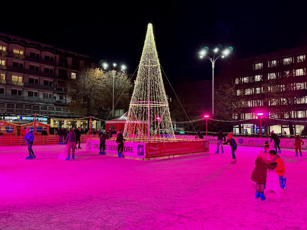 Square skating rink with a triangle shaped tree constructed of white lines in the middle of an Italy city square