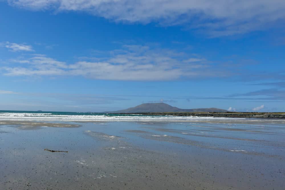 Wide beach at low tide with surf in the distance and a large island on the horizon