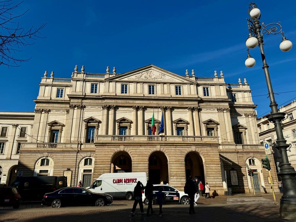 Front of a Baroque style Italian opera house with traffic and a streetlight in front