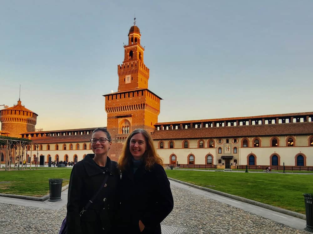 Two women standing in the courtyard of Sforzeco Castle with the Filarete Tower in the background