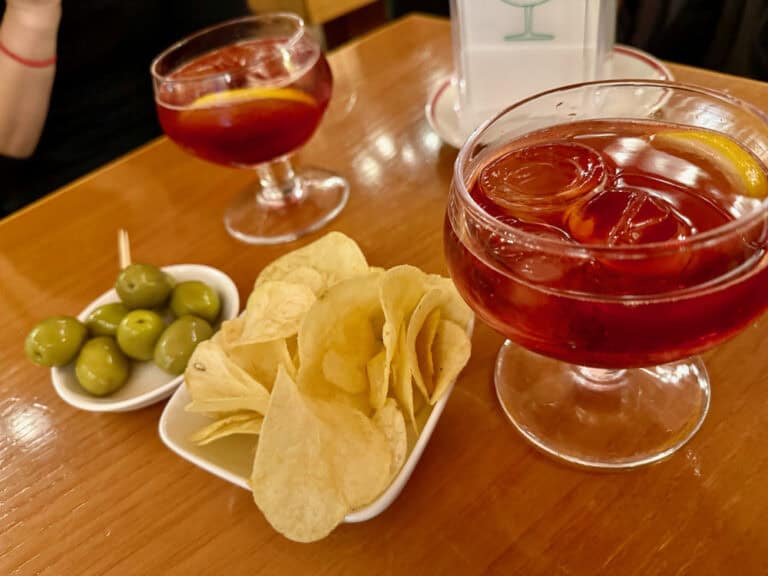 A table top filled with a plate of olives and potato chips as well as two bright red negroni sbagliato aperitivo drinks at Bar Basso Milan