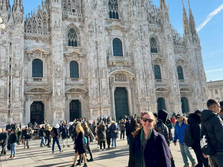 Woman standing in front of crowded pizza and large white marble cathedral in Milan.