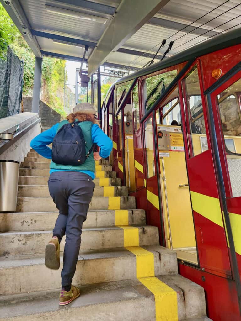 A woman walks up the stairs next to a red and yellow funicular cable car in Lugano Switzerland