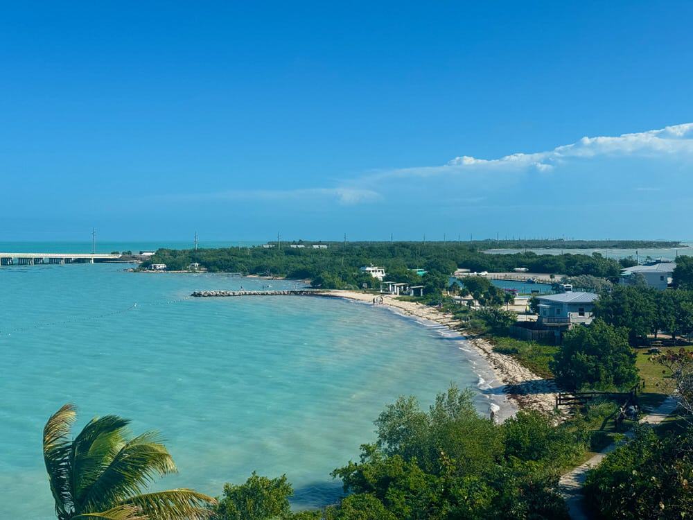 Tropical beach with buildings and a highway bridge crossing an ocean channel.