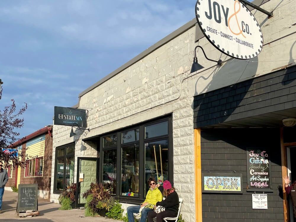 Shoppers sit on a bench outside downtown Grand Marais storefronts on a blue sky October afternoon