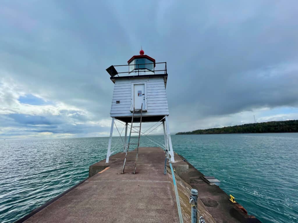 White lighthouse sits at the end of a concrete pier in Lake Superior