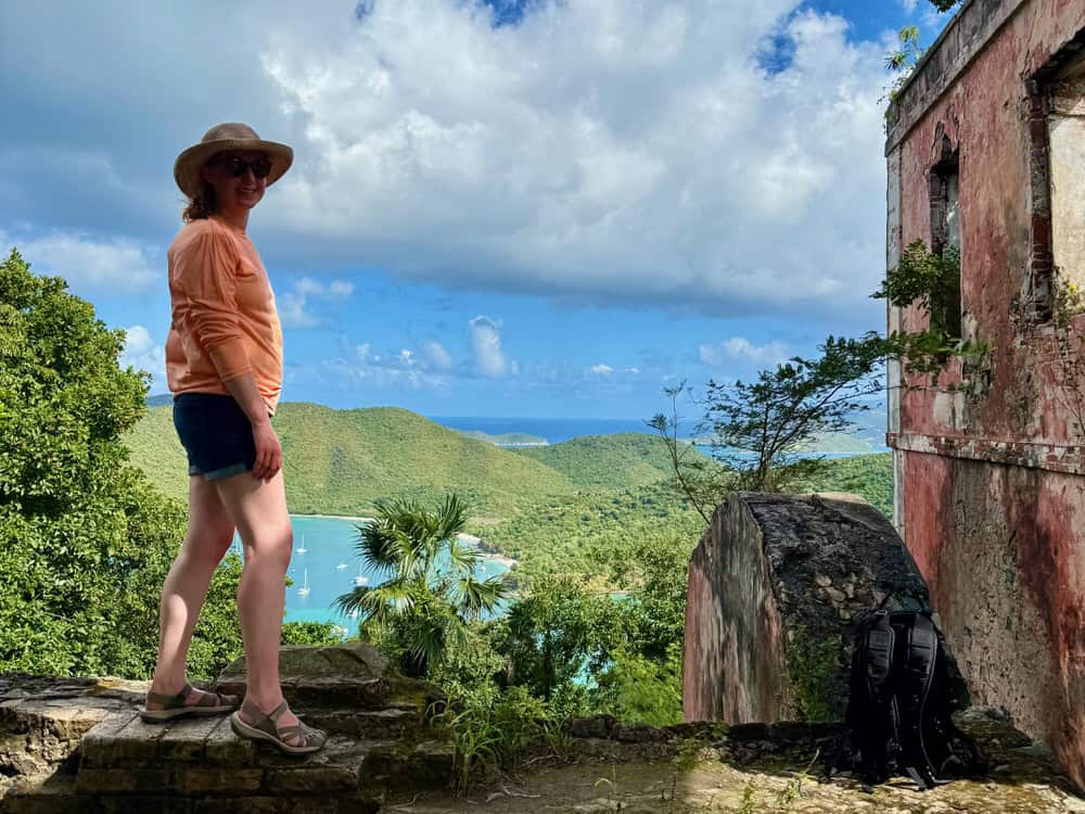 Woman stands on the wall of a ruined estate house at the top of American Hill overlooking Maho and Francis Bays on St. John USVI