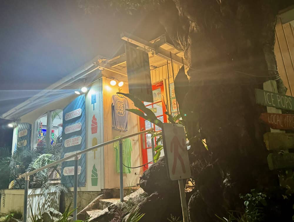 White and blue shop covered with colorful signs lit up after dark. in Cruz Bay
