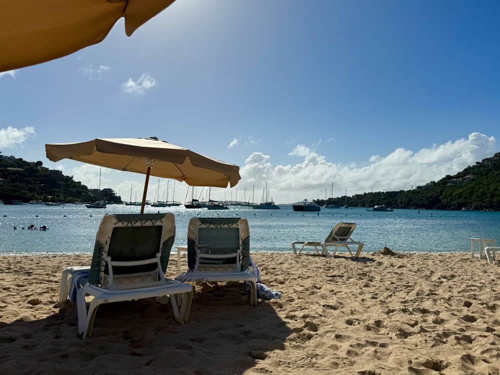 Beach chairs and umbrellas sit on a sandy beach in front of a Caribbean bay