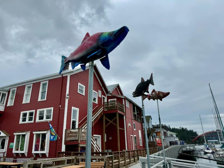 A row of metal fish sculptures on poles in front of a red waterfront building in the Pacific Northwest