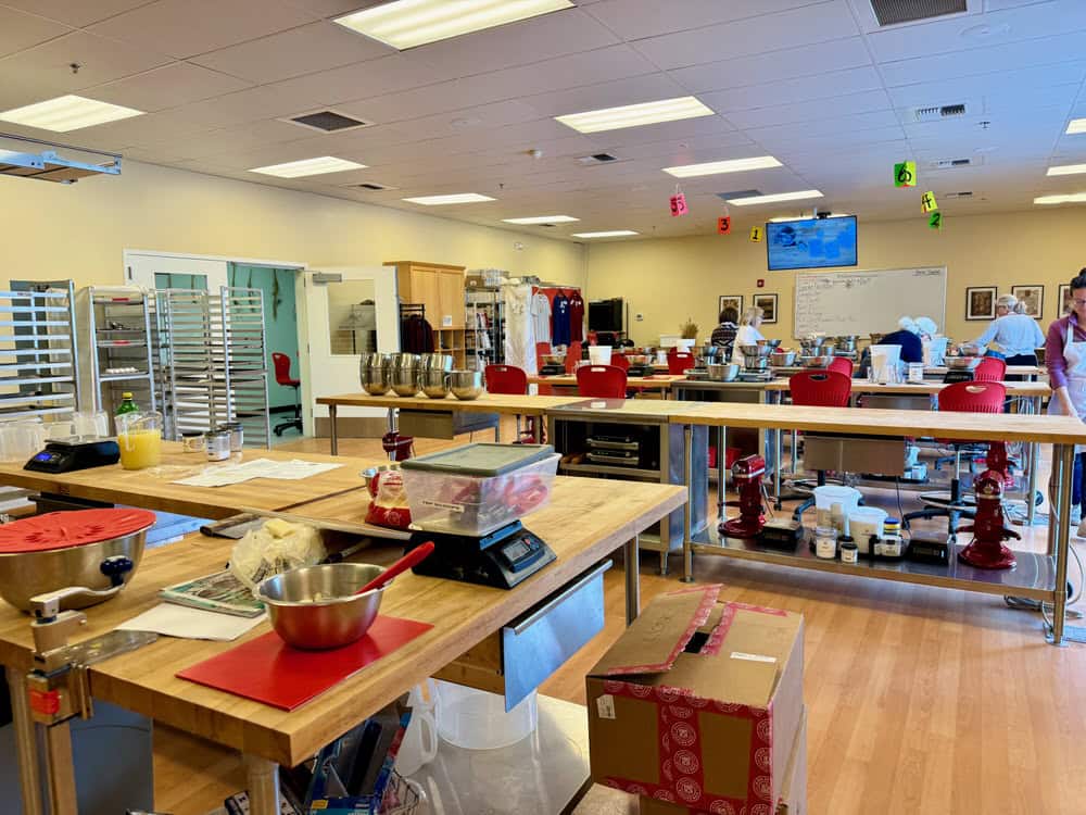 A brightly lit culinary classroom with people milling about before the class