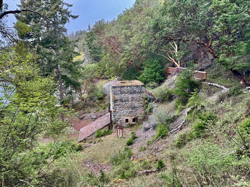 A large stone lime kiln in the middle of a forested shoreline.