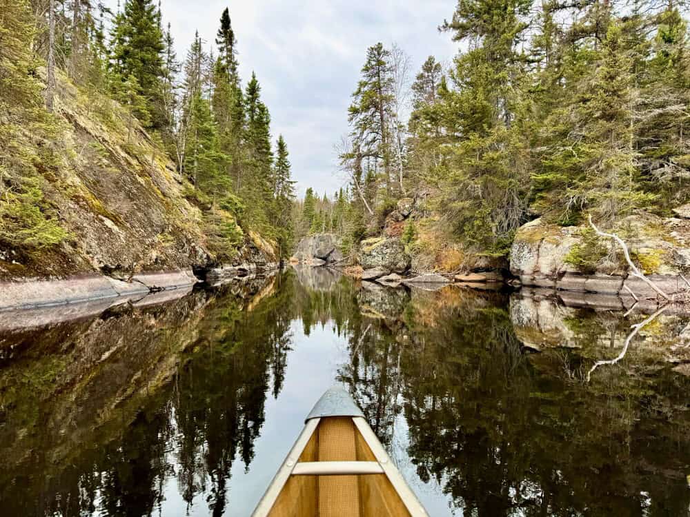 Bow of a Kevlar canoe on a lake pointed towards a canyon of trees.
