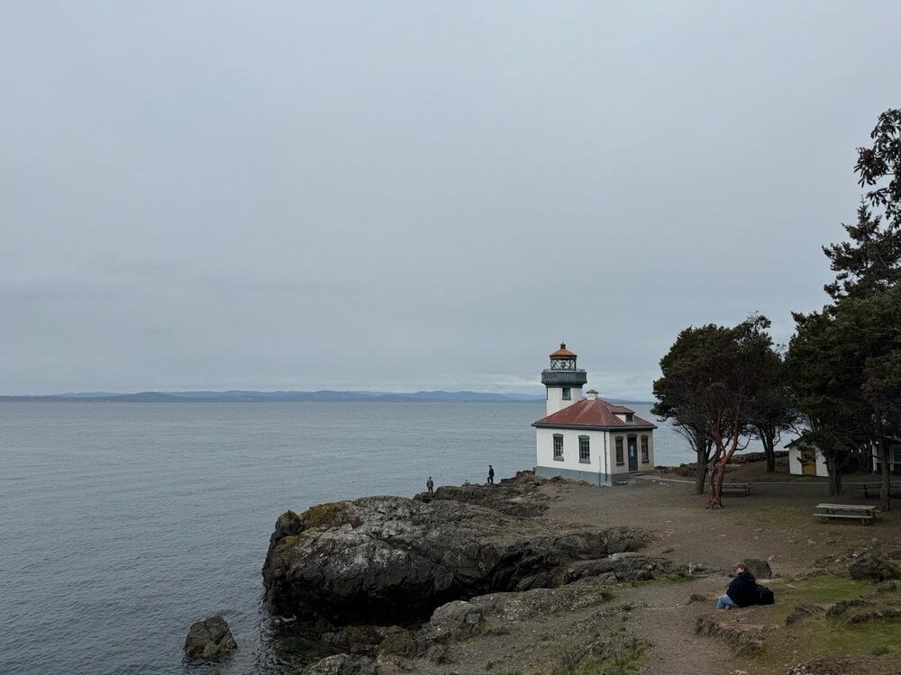 A white lighthouse with a red roof sits on a bluff overlooking the ocean