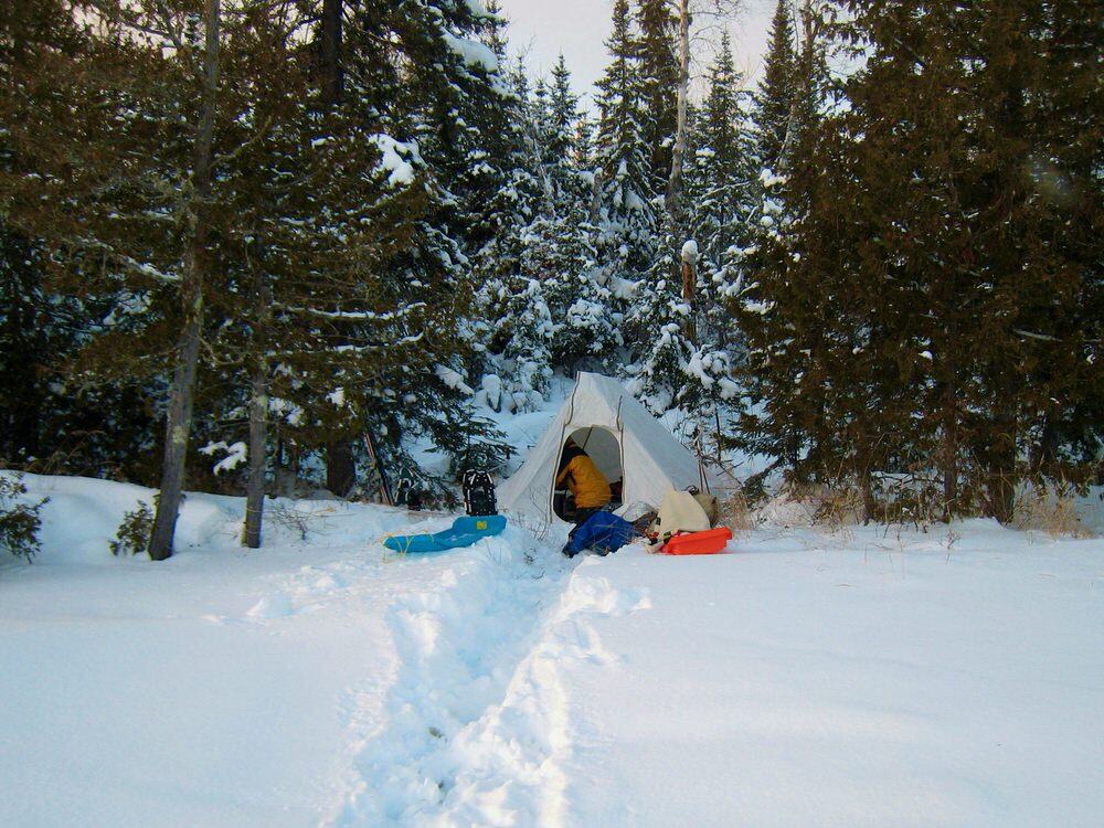 Winter camping tent with sleds in front of it on a frozen Boundary Waters lake shoreline.