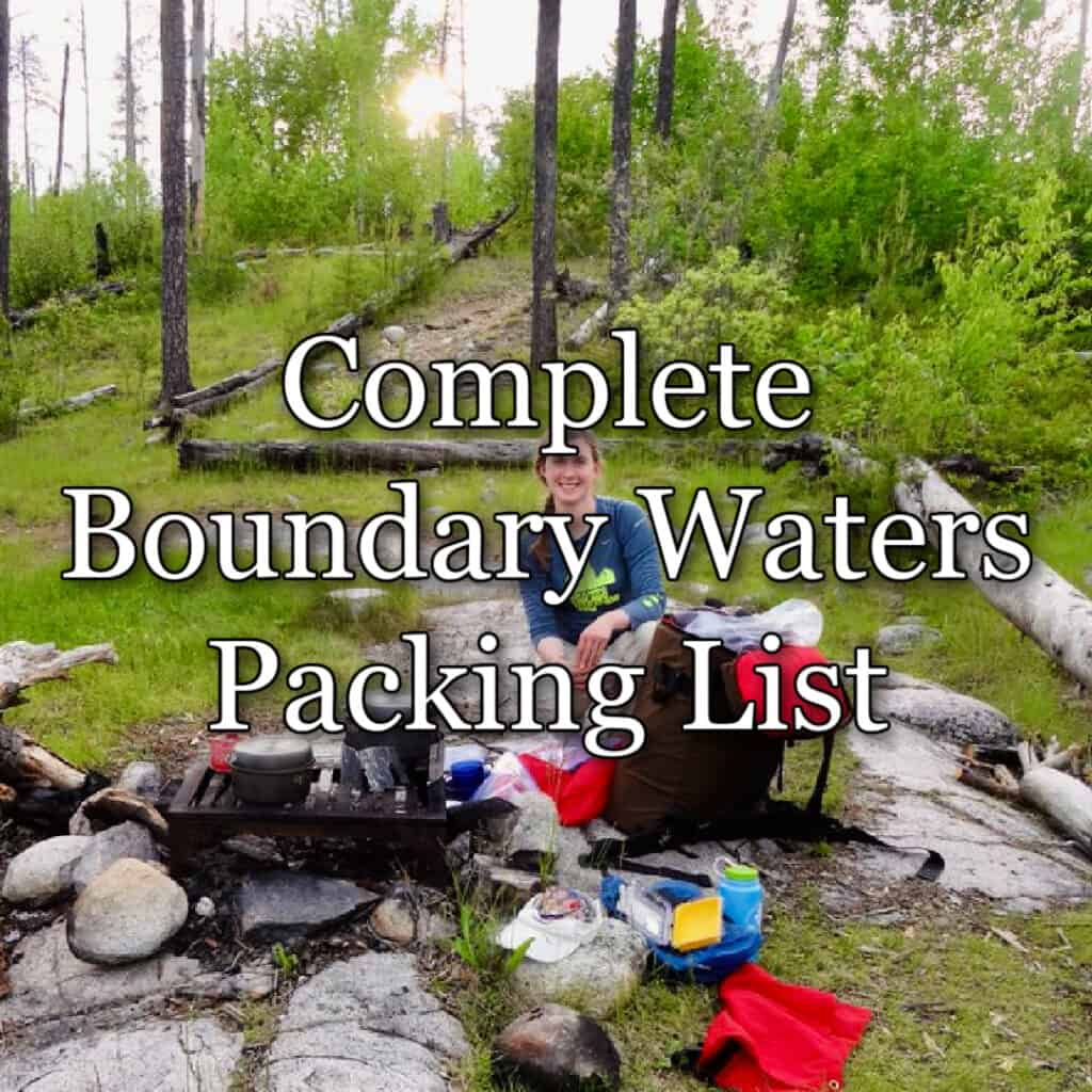Woman kneels in a Boundary Waters campsite surrounded by camping gear.