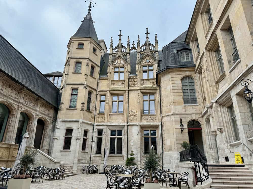 Courtyard of a 15th century stone mansion in Rouen set up with tables and chairs for dining.