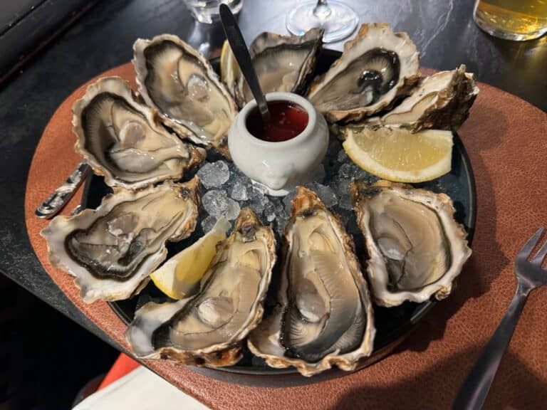 A platter of oysters with lemon wedges and a pot of vinegarette.