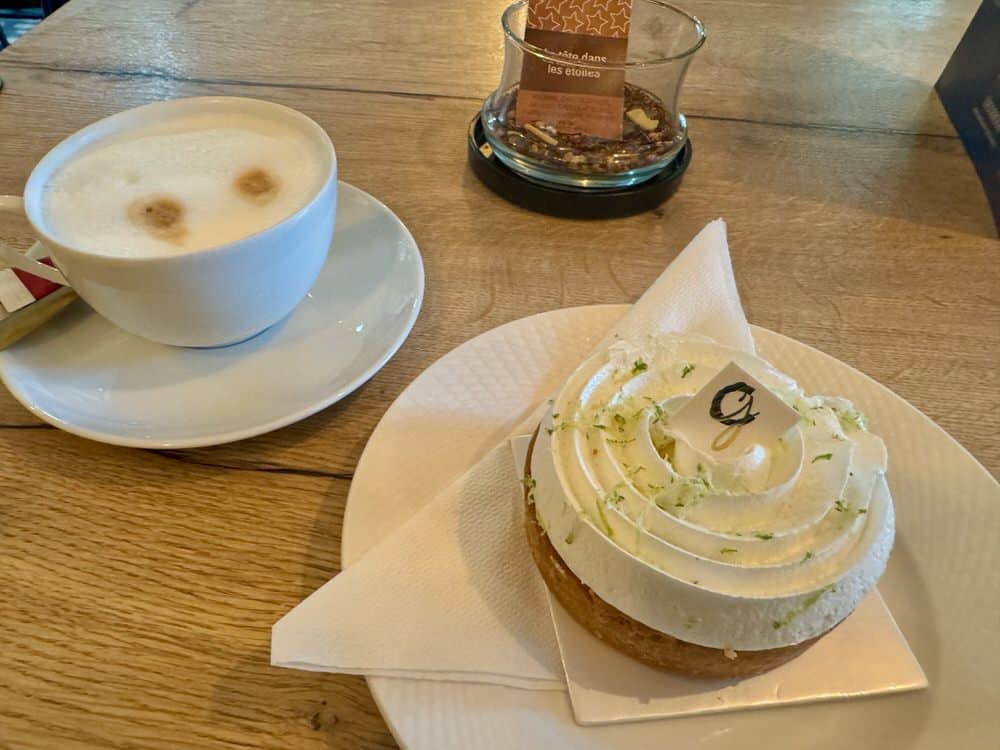 A cup of coffee and an individual sized tart covered in meringue and citrus zest sitting on a wooden table top.