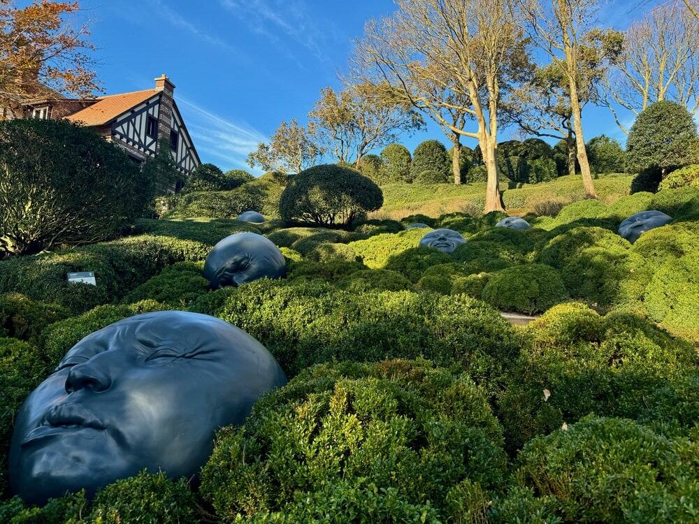 Round black face sculptures tucked amid hedges