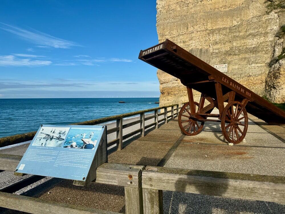 An old wooden diving board on wheels sits on display next the sea