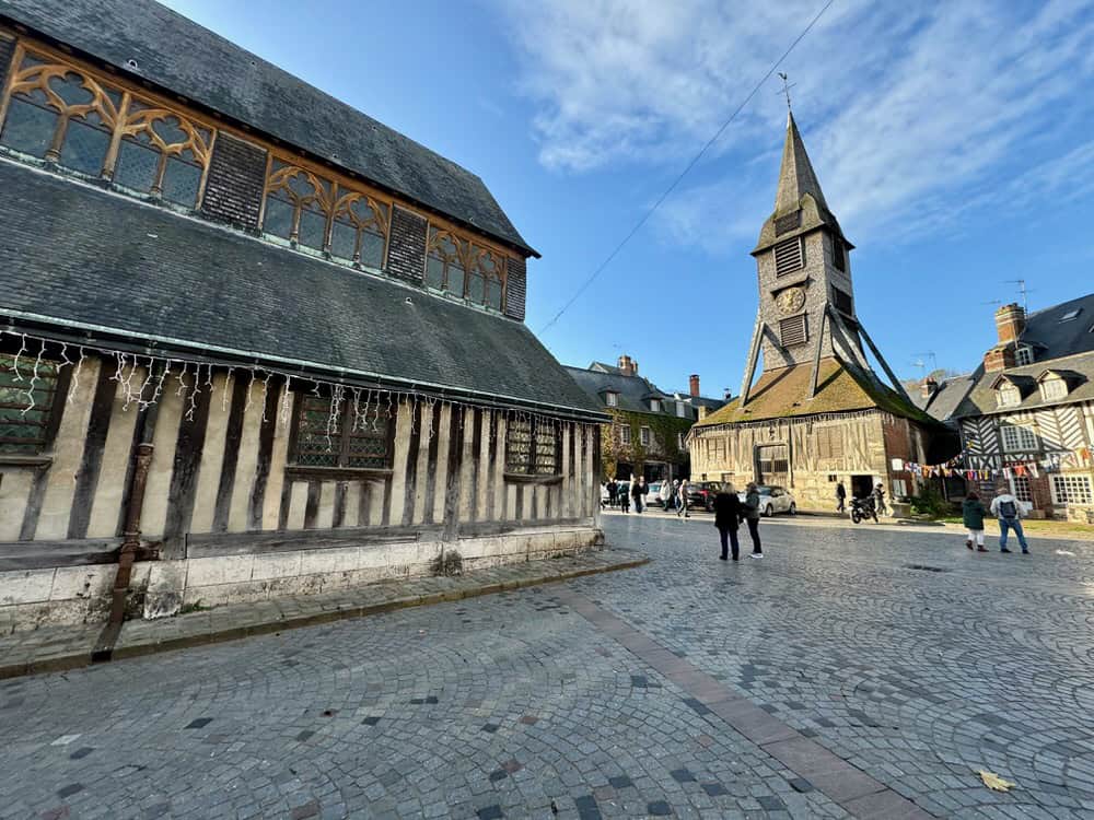 A half timbered church and extant bell tower in a cobblestone square in northern France