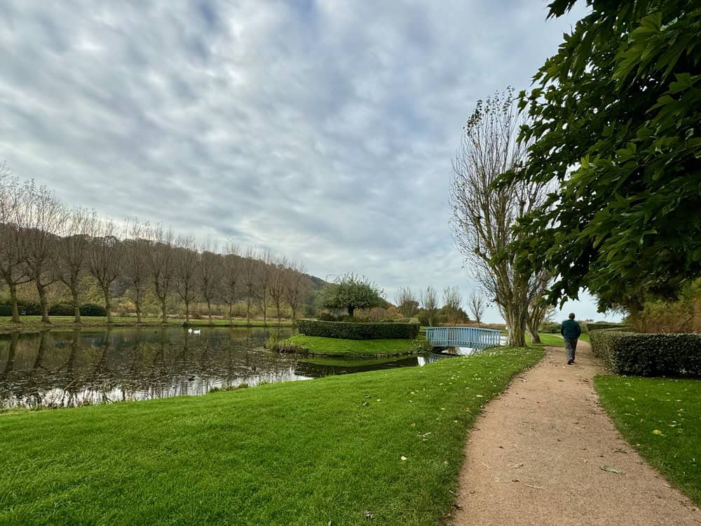 A man walks on a wide path near a pond in a large Honfleur park
