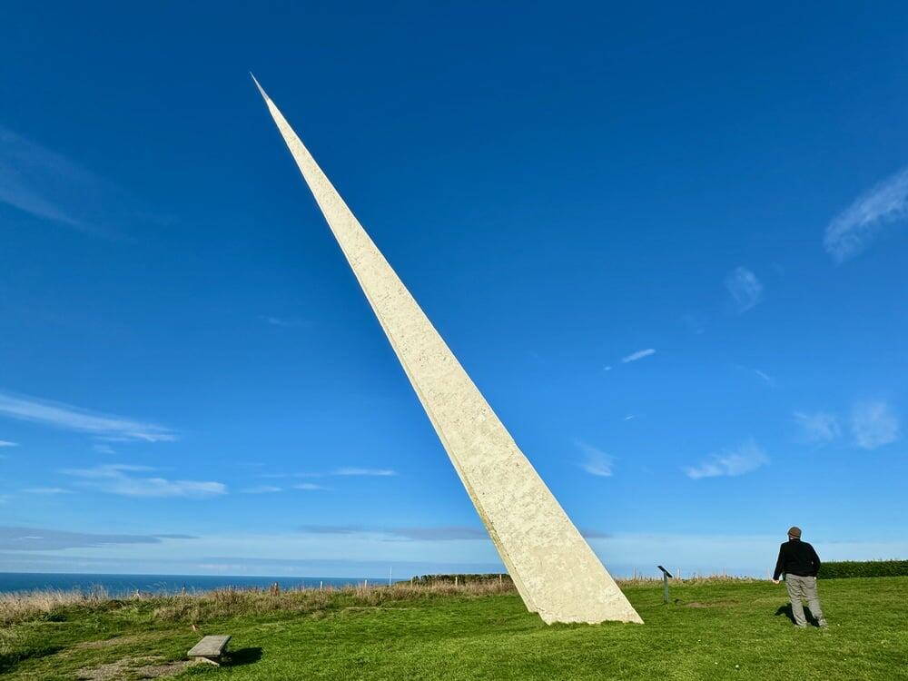 Man looks at a pointy white memorial in a grassy field
