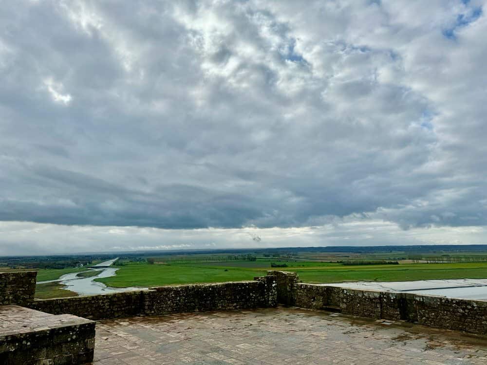 Looking across stone ramparts looking towards a river and flat, green countryside.