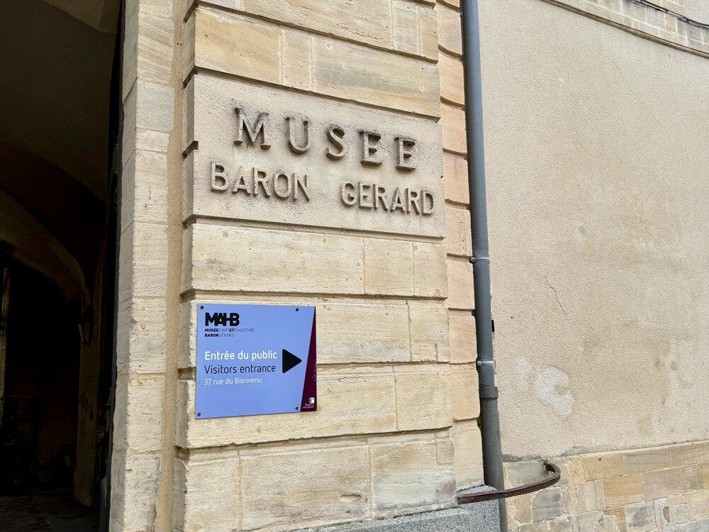 White stone wall with signage for Musee Baron Gerard in downtown Bayeux