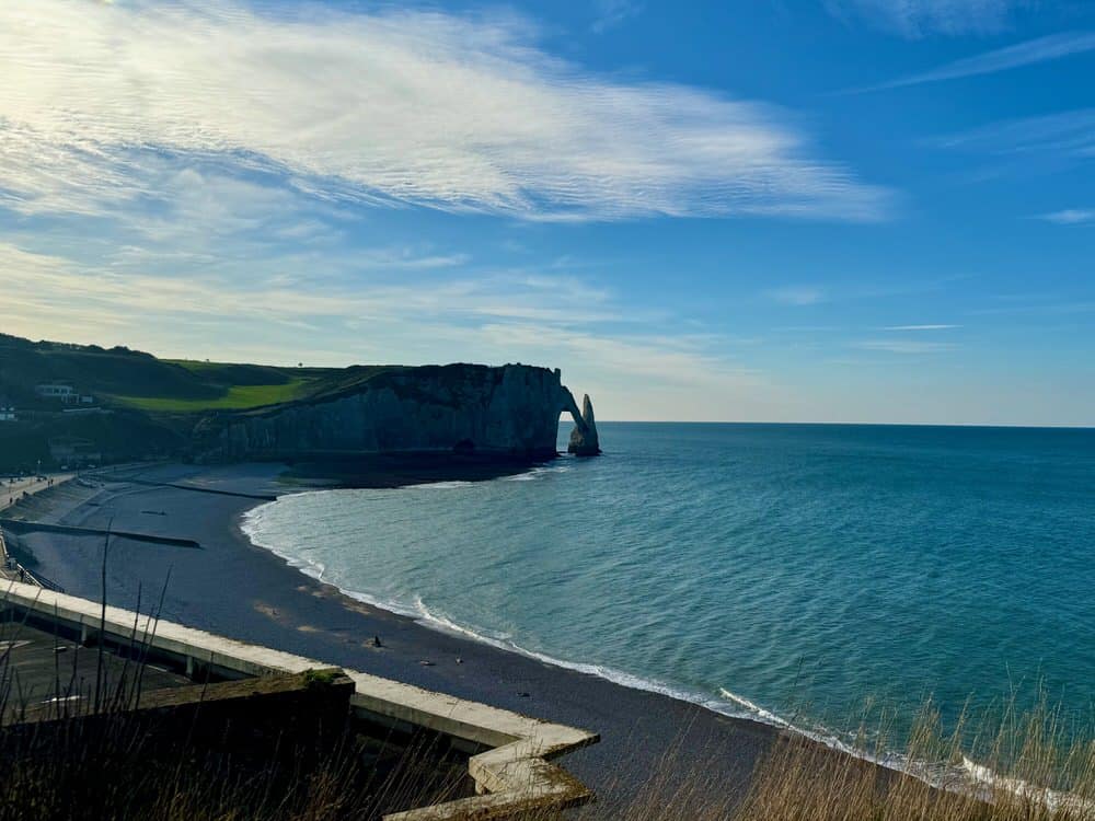 A birds eye view of a dark pebble beach and white chalk cliffs